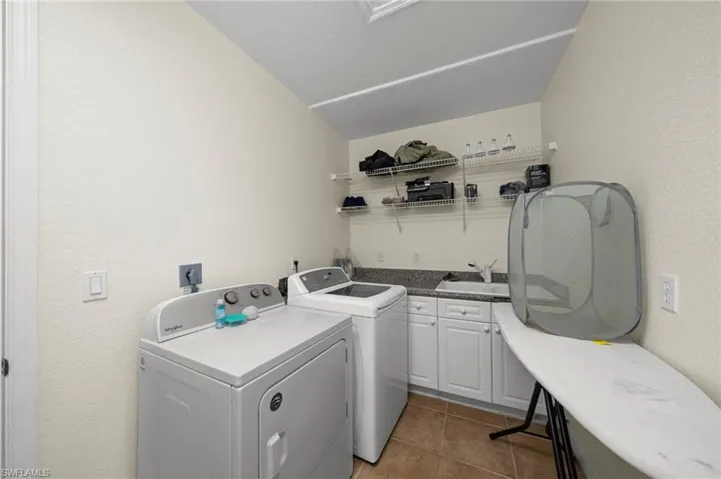 Laundry room featuring a textured wall, washer and clothes dryer, light tile patterned floors, and cabinet space