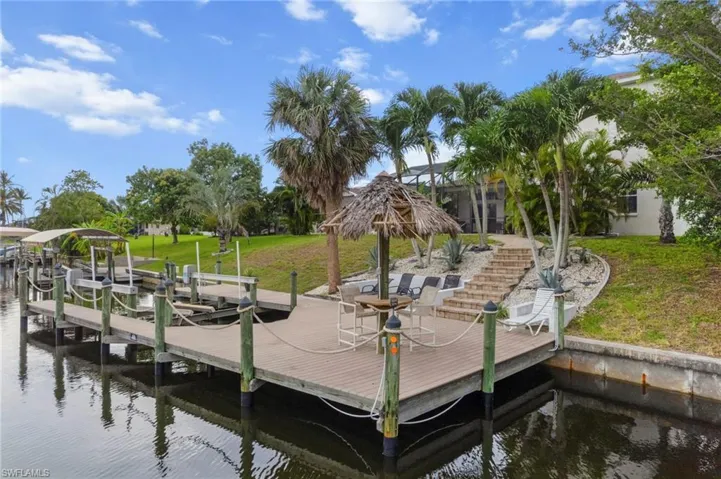 Dock featuring boat lift, a water view, a yard, and a patio
