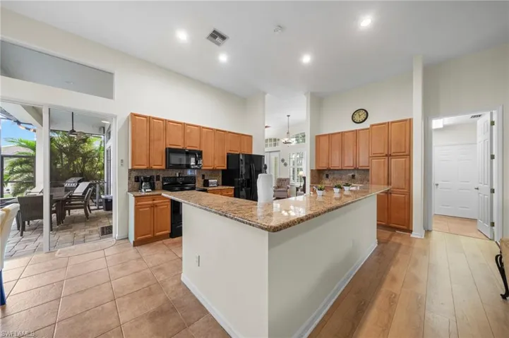 Kitchen featuring backsplash, light stone counters, black appliances, a spacious island, and a high ceiling