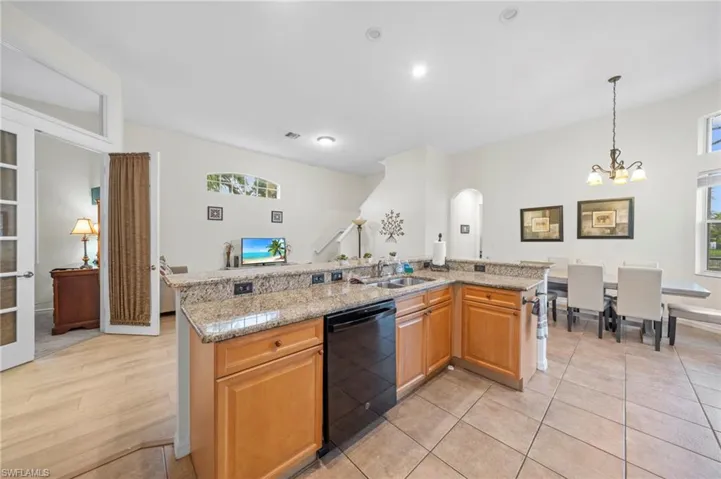 Kitchen with an island with sink, light stone counters, dishwasher, and hanging lights