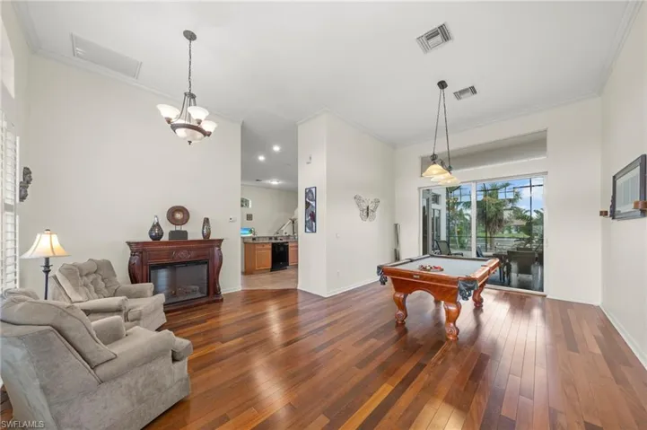 Recreation room featuring dark wood finished floors, ornamental molding, billiards table, a glass covered fireplace, and hanging lights