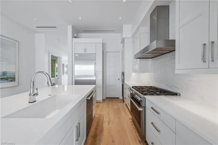 Kitchen featuring high end appliances, backsplash, white cabinets, wall chimney range hood, and sink