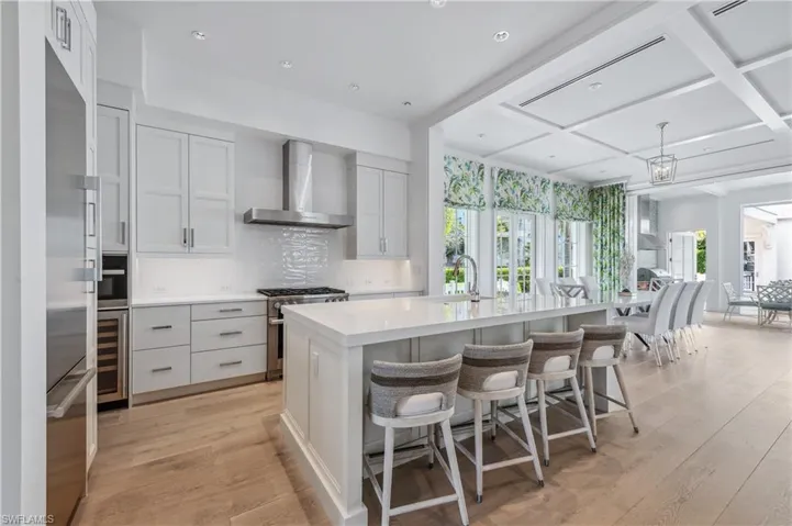 Kitchen featuring a kitchen breakfast bar, wall chimney exhaust hood, an island with sink, light hardwood / wood-style floors, and stainless steel appliances