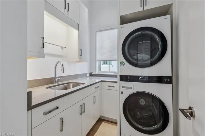 Laundry area featuring sink, cabinets, and stacked washer and clothes dryer