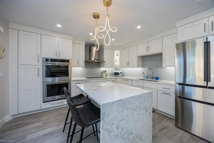 Kitchen featuring sink, appliances with stainless steel finishes, white cabinetry, decorative light fixtures, and wall chimney exhaust hood
