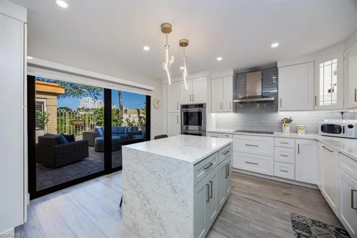 Kitchen with white cabinetry, a center island, decorative backsplash, and wall chimney range hood