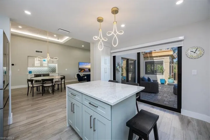 Kitchen featuring pendant lighting, tasteful backsplash, light stone countertops, a kitchen island, and light wood-type flooring