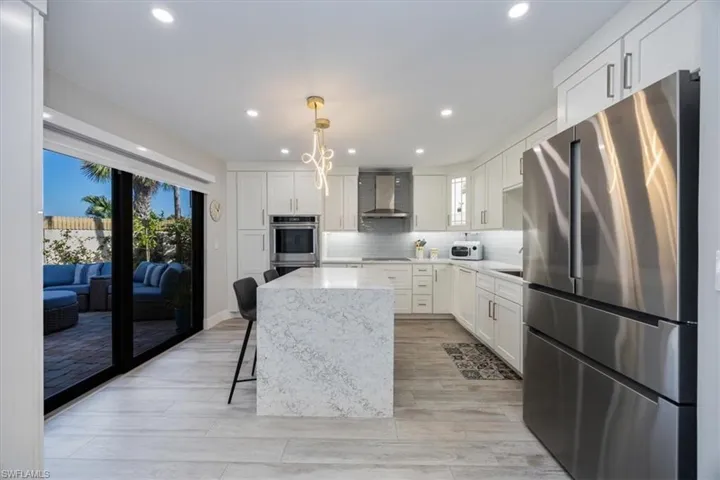 Kitchen with wall chimney range hood, decorative light fixtures, stainless steel appliances, and white cabinets