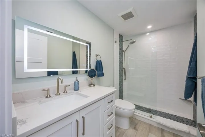 Bathroom featuring vanity, wood-type flooring, toilet, and a tile shower