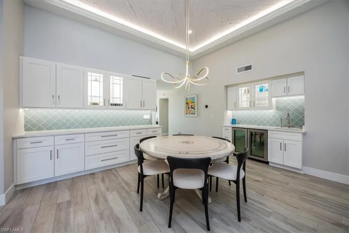 Dining space featuring wine cooler, light hardwood / wood-style floors, a raised ceiling, and sink