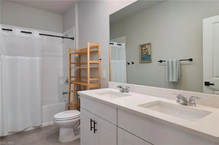 Upstairs bedroom bath featuring tile patterned flooring, toilet, double vanity, and shower / bath combo