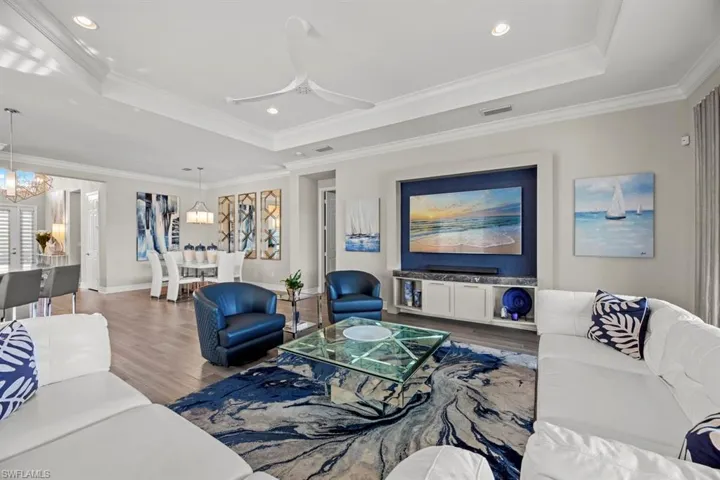 Living room featuring hardwood / wood-style flooring, ceiling fan with notable chandelier, a raised ceiling, and ornamental molding
