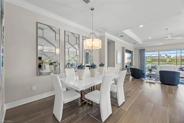 Dining space with a tray ceiling, ceiling fan with notable chandelier, hardwood / wood-style flooring, and crown molding