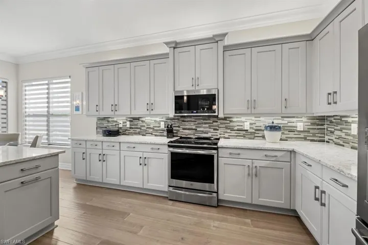 Kitchen featuring stainless steel appliances, light hardwood / wood-style floors, ornamental molding, light stone countertops, and backsplash
