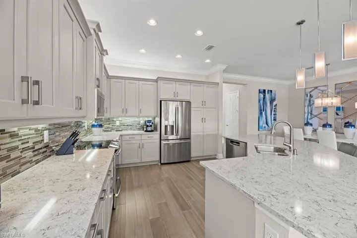Kitchen featuring stainless steel appliances, sink, decorative light fixtures, and light stone counters