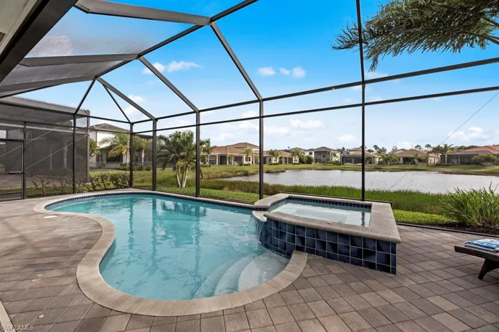 View of pool with glass enclosure, a water view, a patio, and an in ground hot tub