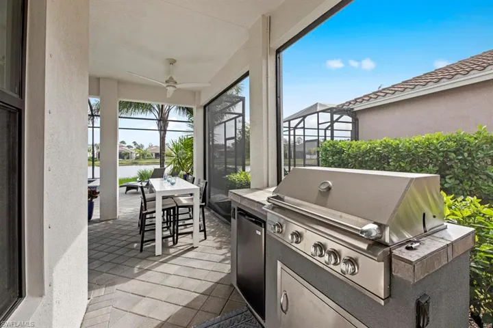 View of patio featuring a water view, exterior kitchen, a grill, ceiling fan, and a lanai