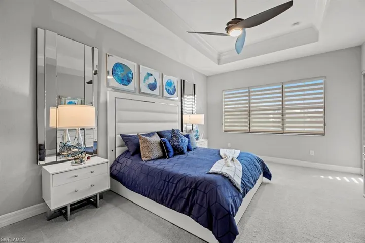 Carpeted bedroom with ornamental molding, ceiling fan, and a tray ceiling