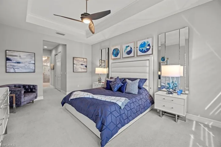 Bedroom with light colored carpet, ceiling fan, connected bathroom, and a tray ceiling