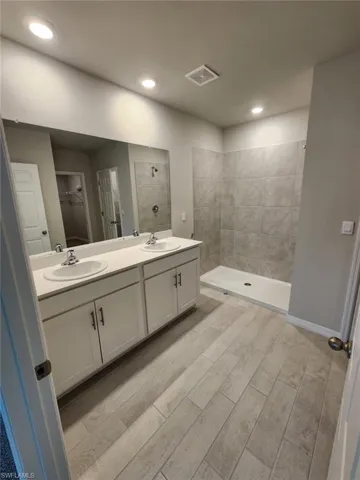 Bathroom with a walk in closet, double vanity, a stall shower, wood finish floors, and recessed lighting