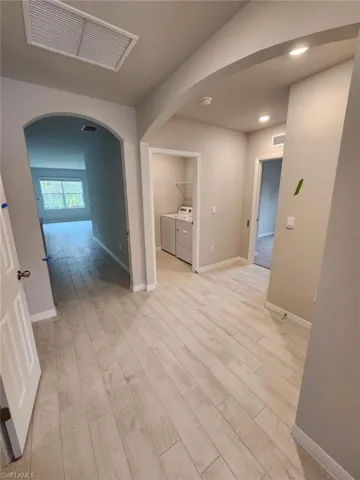 Hallway with arched walkways, independent washer and dryer, and light wood-type flooring