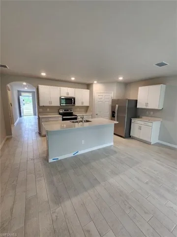 Kitchen with appliances with stainless steel finishes, arched walkways, recessed lighting, white cabinets, and a kitchen island with sink
