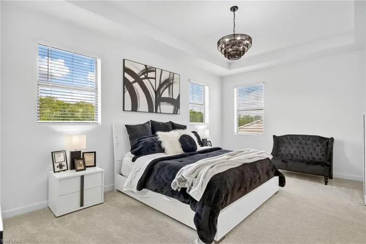 Bedroom with light carpet, multiple windows, and a chandelier