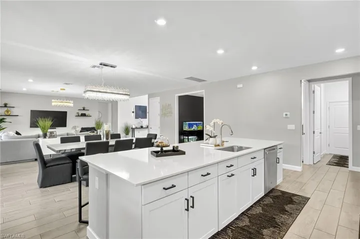 Kitchen featuring open floor plan, a kitchen island with sink, wood finish floors, white cabinetry, and light countertops