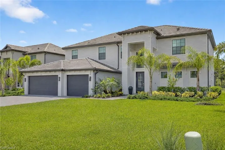 View of front facade with a front yard, an attached garage, driveway, a tile roof, and stucco siding