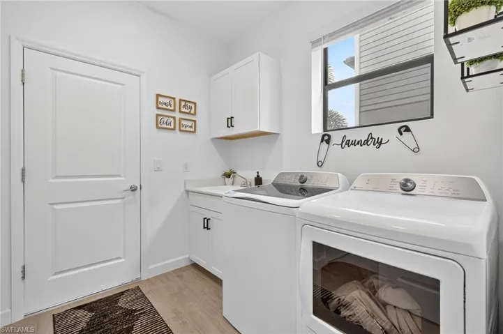 Laundry area with independent washer and dryer, light wood finished floors, and cabinet space