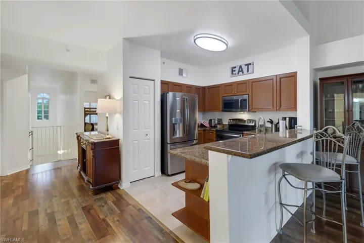 Kitchen with light wood-type flooring, dark stone counters, stainless steel appliances, a kitchen breakfast bar, and kitchen peninsula