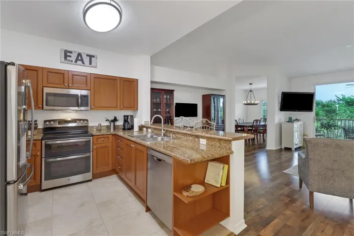 Kitchen with appliances with stainless steel finishes, kitchen peninsula, sink, light stone counters, and light wood-type flooring