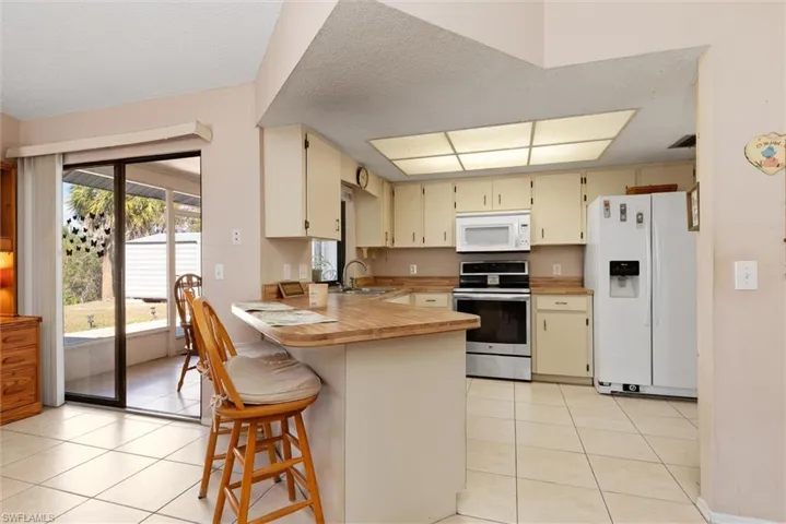 Kitchen with cream cabinetry, white appliances, a peninsula, a kitchen bar, and light tile patterned flooring