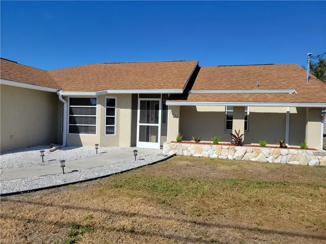 View of exterior entry with stucco siding, a lawn, and roof with shingles