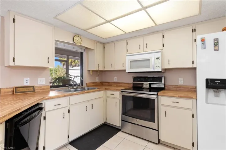 Kitchen featuring white appliances, cream cabinets, light tile patterned floors, and wooden counters