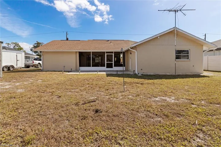 Back of house with a yard, stucco siding, a sunroom, and roof with shingles