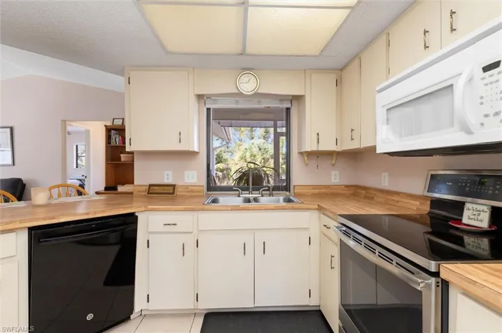 Kitchen with stainless steel range with electric stovetop, white microwave, dishwasher, cream cabinets, and butcher block counters