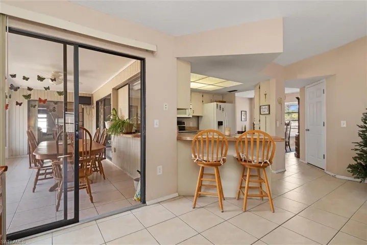 Kitchen with a breakfast bar, white appliances, cream cabinetry, a peninsula, and light tile patterned floors