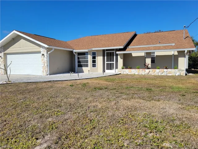 Ranch-style home with a front lawn, an attached garage, roof with shingles, and stucco siding