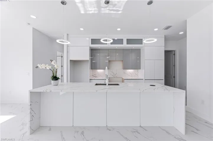 Kitchen with gray cabinetry, decorative backsplash, sink, and hanging light fixtures