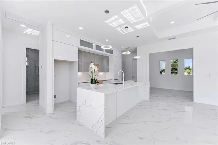Kitchen featuring pendant lighting, white cabinets, sink, an island with sink, and light stone counters