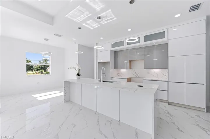 Kitchen featuring gray cabinetry, sink, backsplash, pendant lighting, and a center island with sink