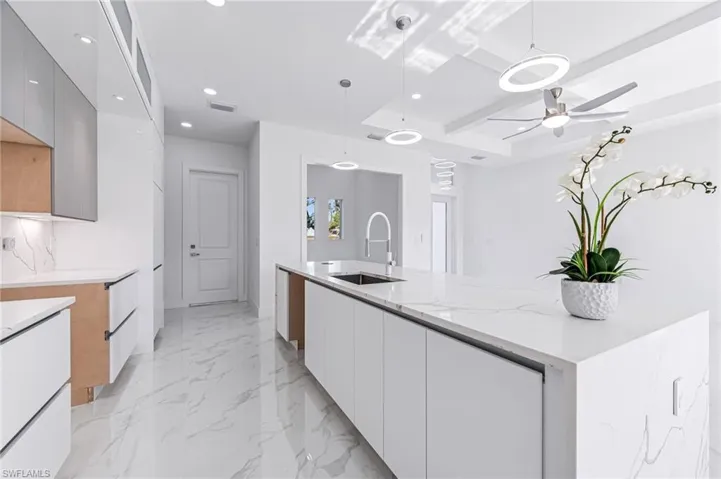 Kitchen with light stone counters, gray cabinetry, ceiling fan, sink, and pendant lighting