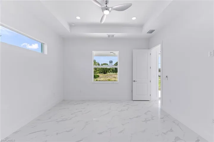 Spare room featuring a raised ceiling, plenty of natural light, and ceiling fan