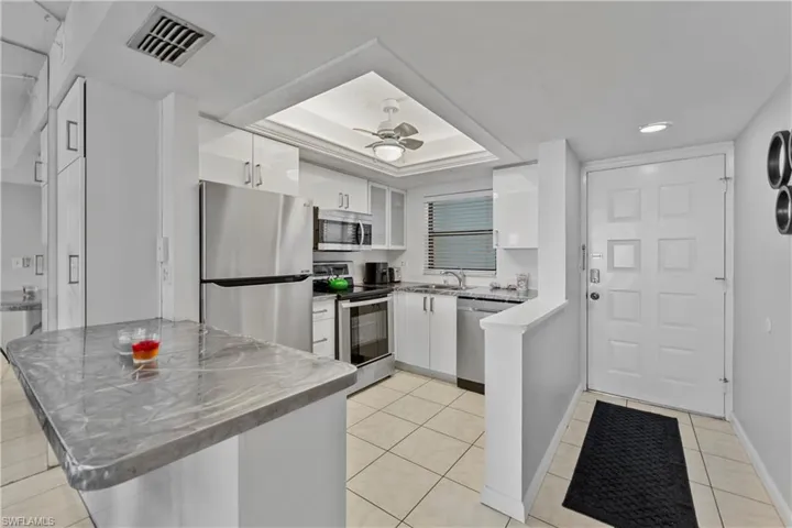 Kitchen with stainless steel appliances, a peninsula, white cabinetry, ceiling fan, and a raised ceiling