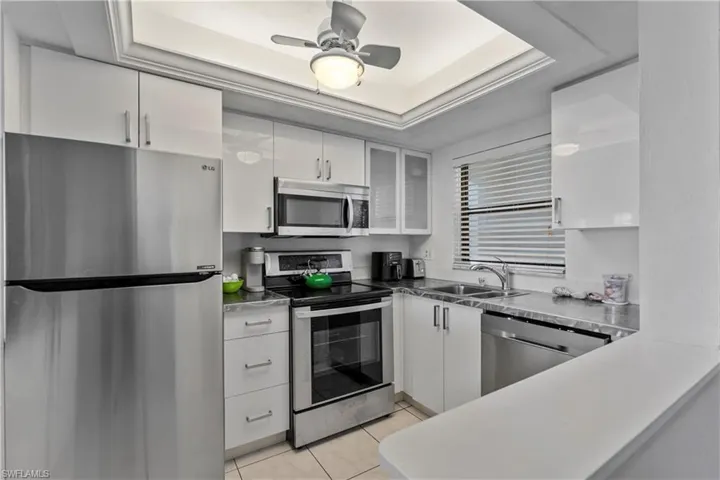 Kitchen featuring appliances with stainless steel finishes, a tray ceiling, white cabinetry, a ceiling fan, and light tile patterned floors