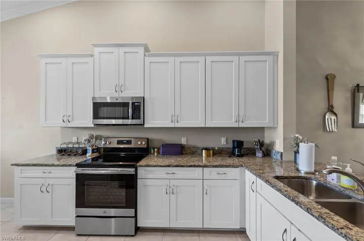 Kitchen featuring white shaker-style cabinetry, granite countertops, and stainless steel appliances including an oven range and built-in microwave