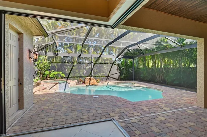View of pool featuring a lanai, a patio, a pool with connected hot tub, and a sunroom