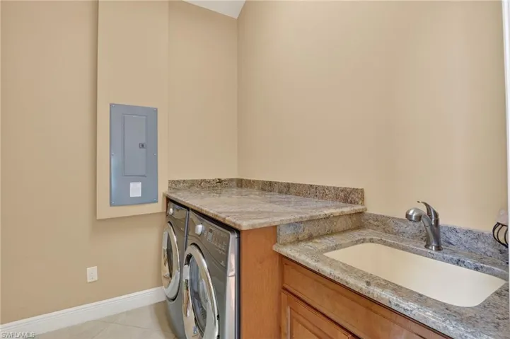 Laundry area featuring electric panel, washing machine and clothes dryer, and light tile patterned floors