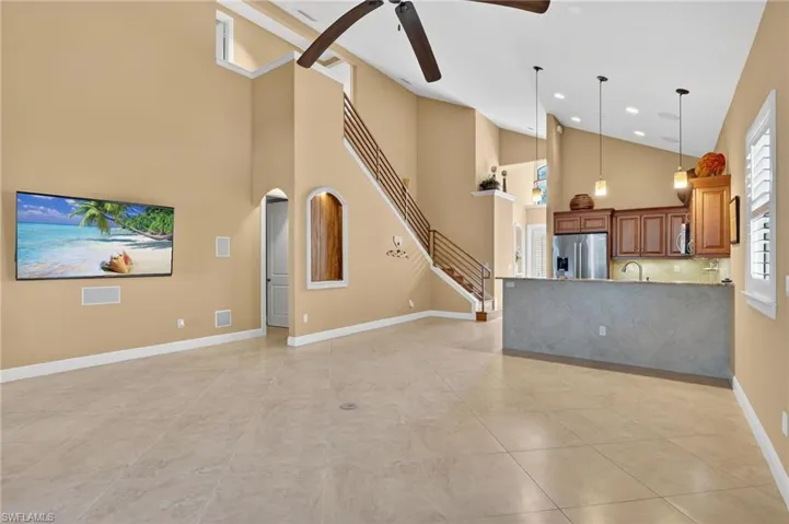 Unfurnished living room with ceiling fan, high vaulted ceiling, stairway, and light tile patterned flooring